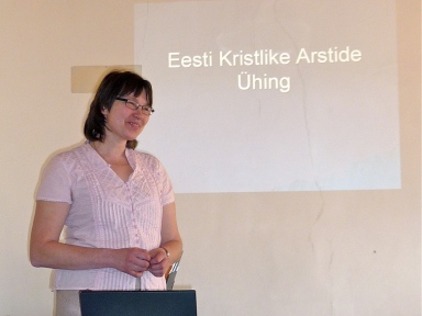 Mirjam Türkson seismas ekraani ees kus on tiitelslaid tekstiga "Eesti Kristlike Arstide Ühing"